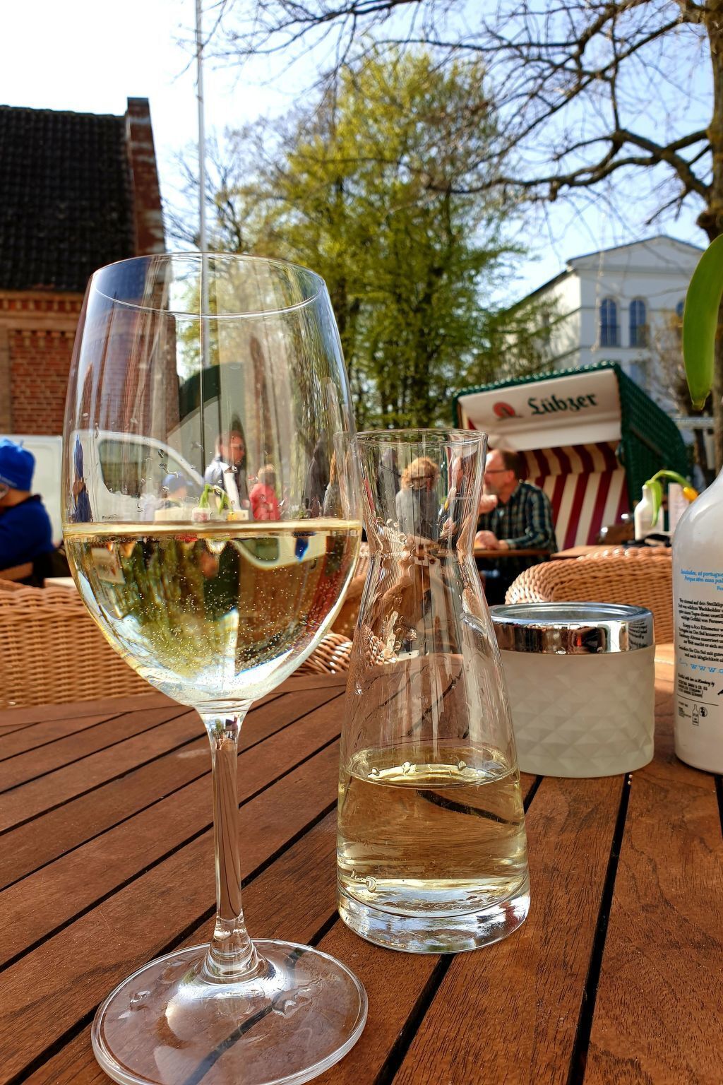 Un verre de vin blanc sur une table en bois, avec une bouteille transparente à côté.