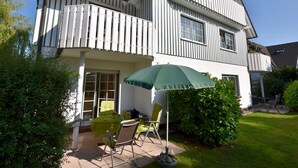 Una casa de dos pisos con un balcón, un patio con muebles de exterior y un paraguas verde.