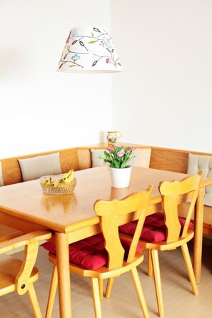 A round wooden dining table with six chairs, a white floral lampshade, a small potted plant, and a bowl of bananas. - FeWo Falkenstein 25 by Interhome (Oberstdorf)