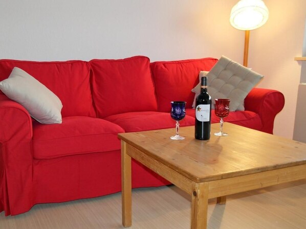 A red sofa with a cushion, a wooden table, two wine glasses, and a bottle of wine. - FeWo Falkenstein 25 by Interhome (Oberstdorf)