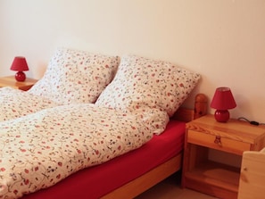 A single bed with a floral bedspread and red pillows, flanked by two wooden nightstands with red lamps. - FeWo Falkenstein 25 by Interhome (Oberstdorf)