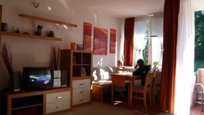 Una sala de estar con televisor, estantería, mesa de comedor con sillas y obras de arte en las paredes.