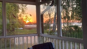 A room with a view of a sunset over a body of water, a white railing, and a towel rack.
