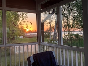 Una habitación con vista al atardecer sobre el agua, una barandilla blanca y un perchero.
