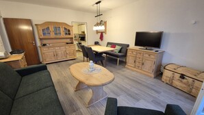 A modern living room with a sofa, a wooden coffee table, a TV, and a dining area with a table and chairs. - Falkenberg Wh 218 by Interhome (Oberstdorf)
