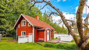 A red house with a white fence, a wooden deck, and a large tree in the foreground. - Vacation home Ida by Interhome (Mariannelund)