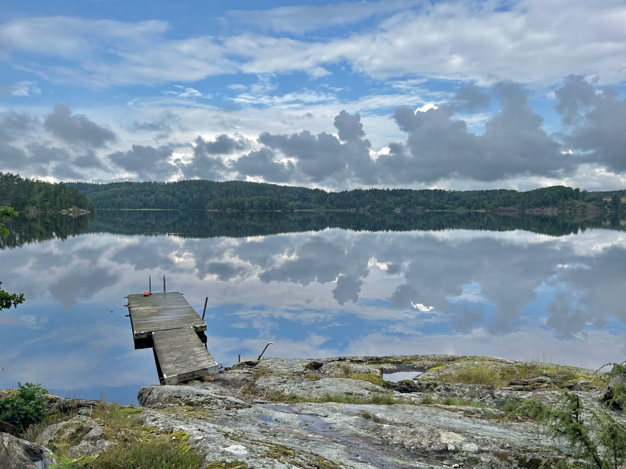 A wooden dock extending into calm lake waters, surrounded by rocky terrain and dense forest.