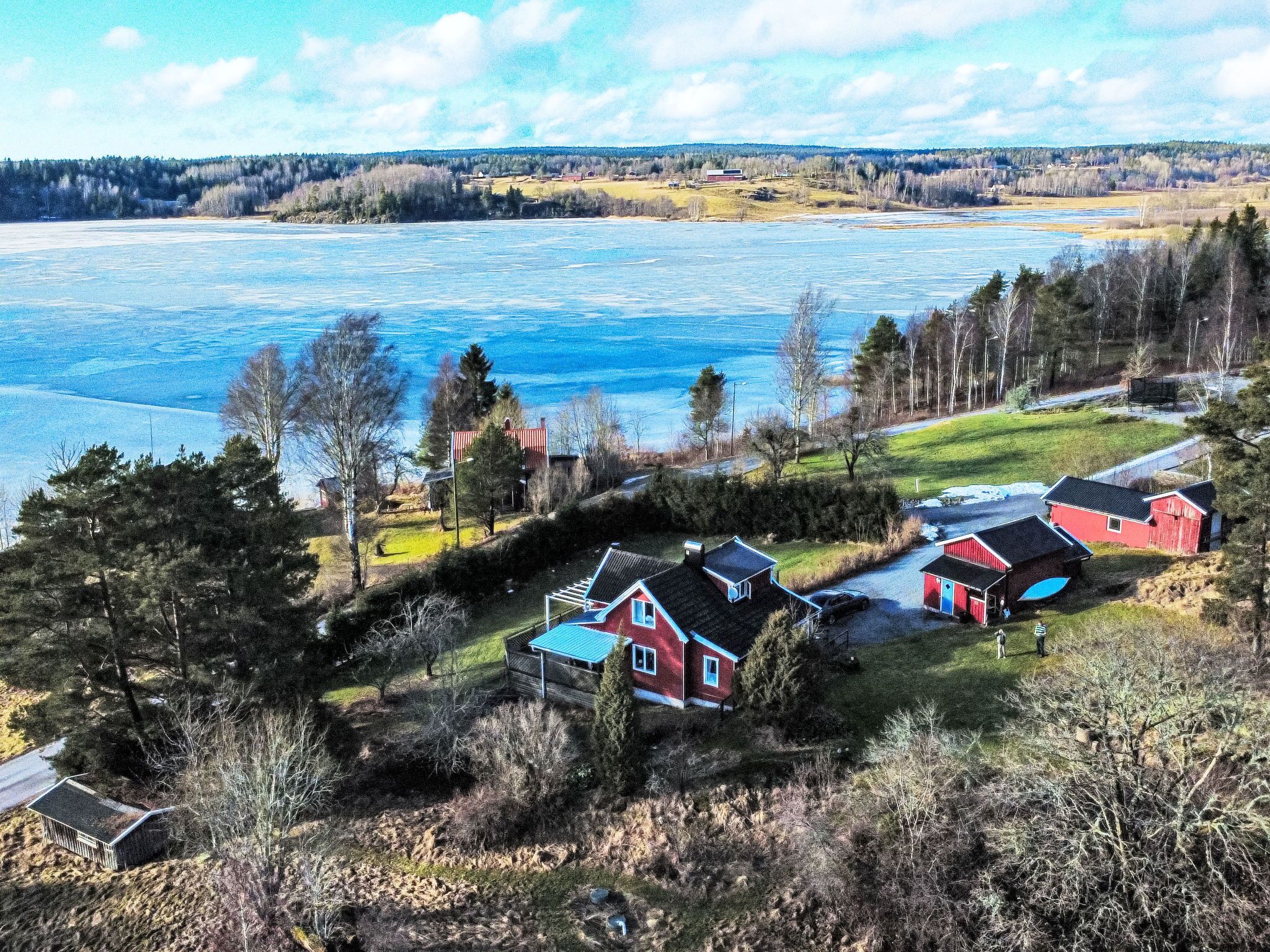 A lakeside property with multiple red buildings, a grassy area, and a forested background.
