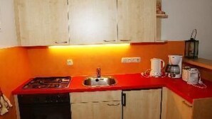 Una cocina funcional con armarios de madera, encimera roja, pileta, estufa y cafetera.