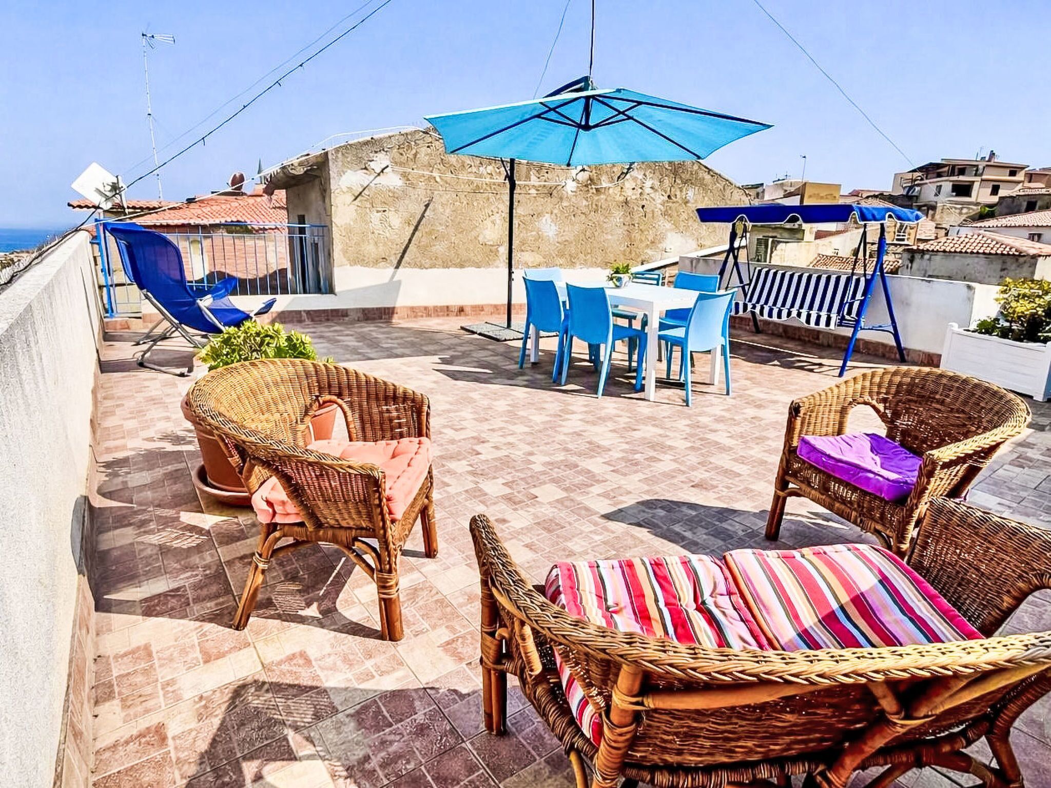 A rooftop terrace with wicker furniture, a table, chairs, and a blue umbrella.