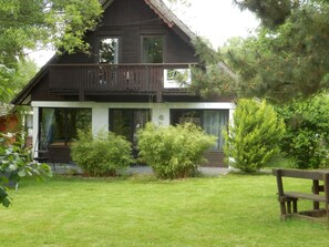 A two-story wooden house with a balcony, surrounded by greenery and a grassy lawn. - mit Grill, Terrasse und Garten by Interhome (Frielendorf)