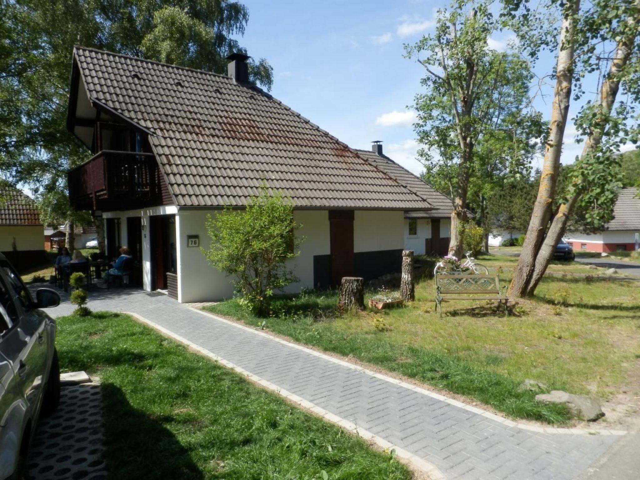 Een huis met twee verdiepingen, een pannendak, een balkon en een verharde oprit.