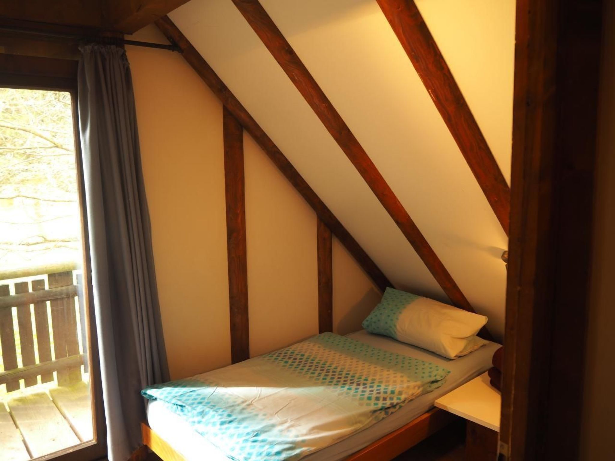 A small, single-bed room with a sloped ceiling and wooden beams.