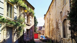 A cobblestone alley between old stone buildings with shutters, a red door, and a parked car.