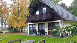 A wooden house with a balcony, a patio with a table and chairs, and a garden with autumn leaves. - Vacation home Tindy by Interhome (Frielendorf)