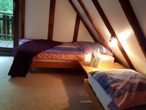 Un dormitorio con techo inclinado, una cama con manta púrpura y una mesita de noche con lámpara.
