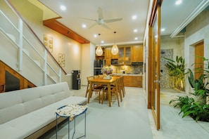 A modern kitchen with wooden cabinets, a dining area with a white sofa and table, and a staircase with a white railing.