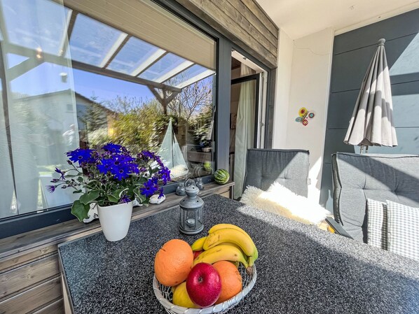 Ein Balkon mit Tisch, Topfpflanzen, Obstschale und Blick ins Freie.