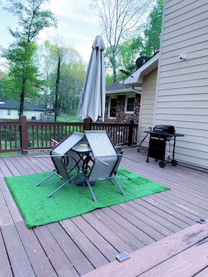 Eine Terrasse mit Tisch, Stühlen, einem Grill und einem Sonnenschirm.