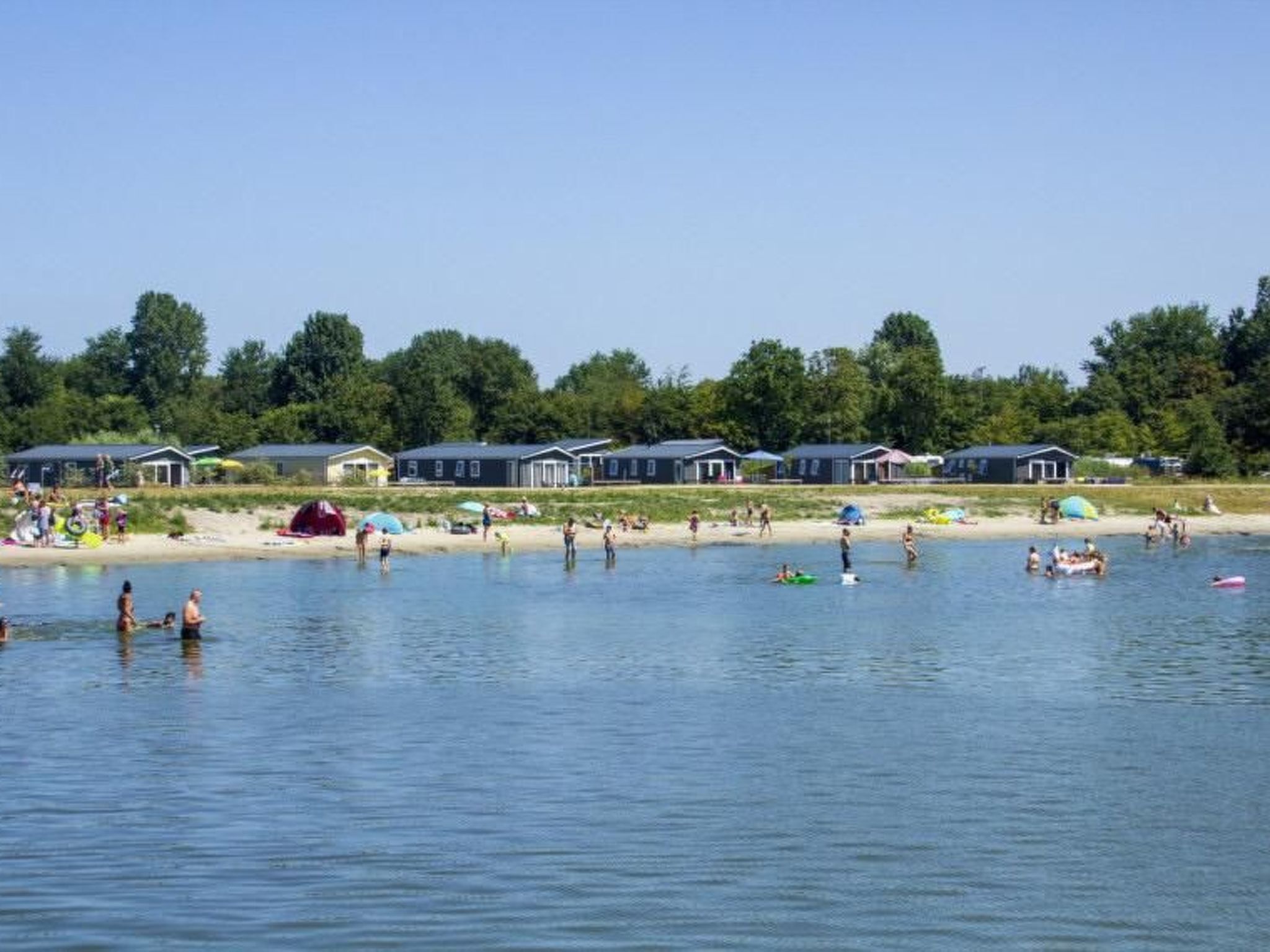 Ein Ferienresort am Seeufer mit mehreren Blockhütten, einem Sandstrand und Personen, die Wassersport betreiben.