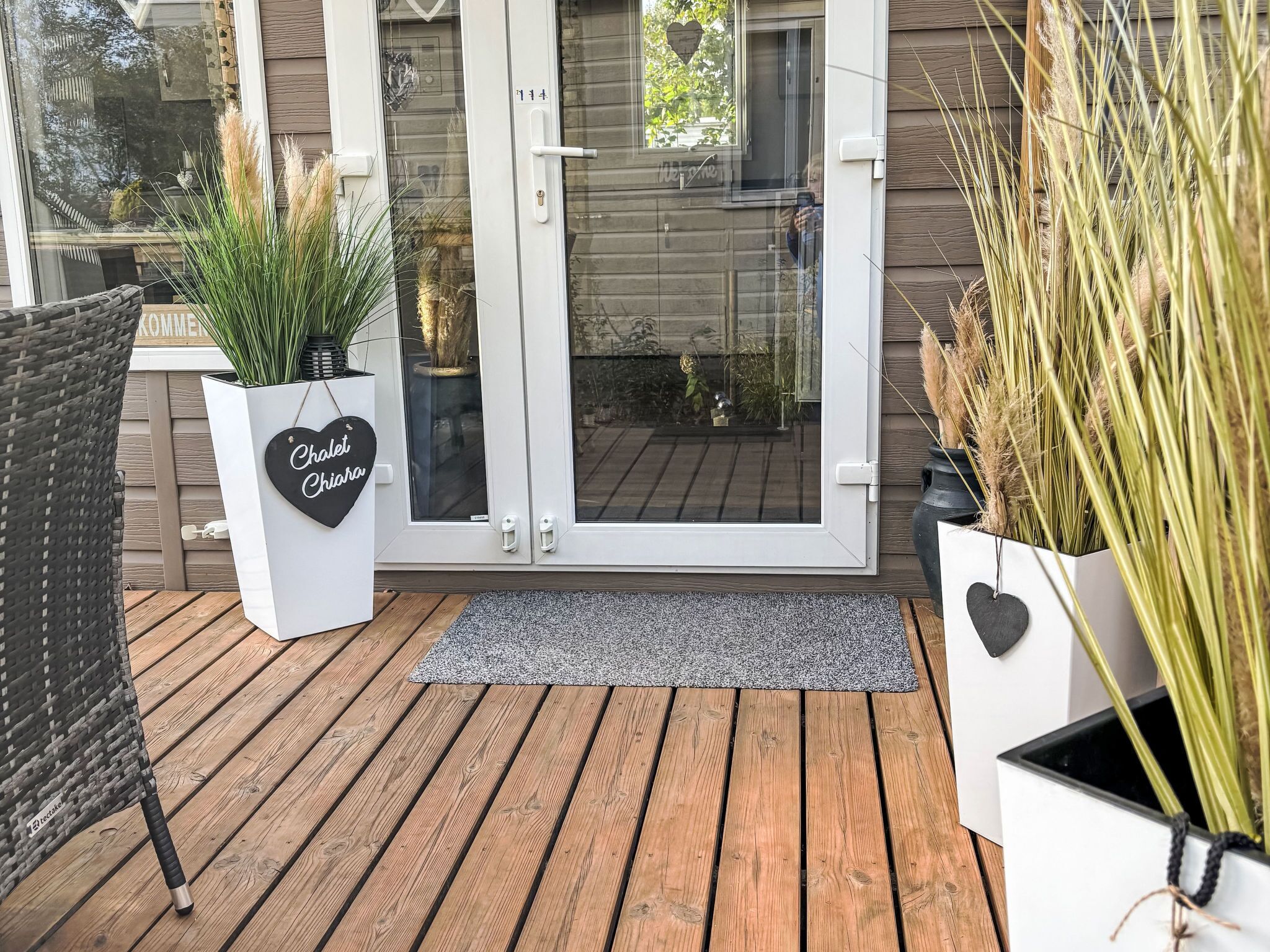 Eine Holzterrasse mit Glastür, Topfpflanzen und einem Korbstuhl.