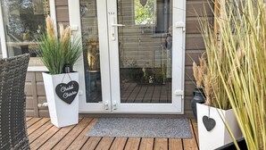 En träaltan med en glasdörr, krukväxter och en flätad stol.