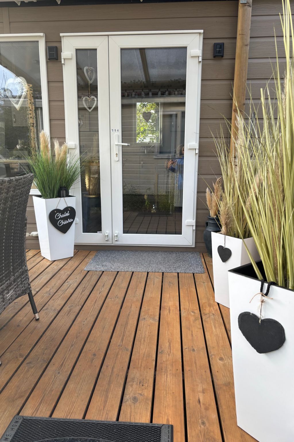 Eine Holzterrasse mit Glastür, Kübelpflanzen und einem Korbstuhl.