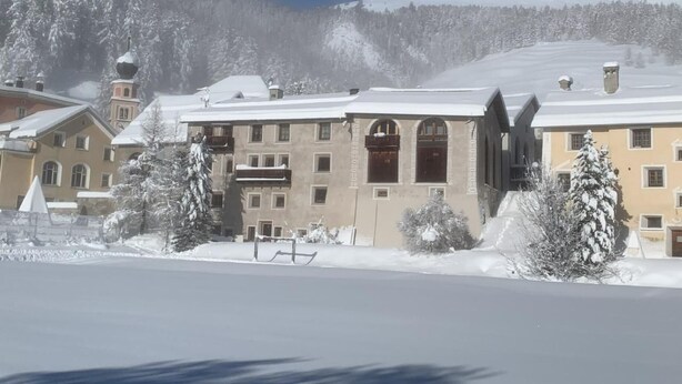 Ein mit Schnee bedecktes Gebäude mit zahlreichen Fenstern und Balkonen, umgeben von schneebedeckten Bäumen und einem Berg im Hintergrund.