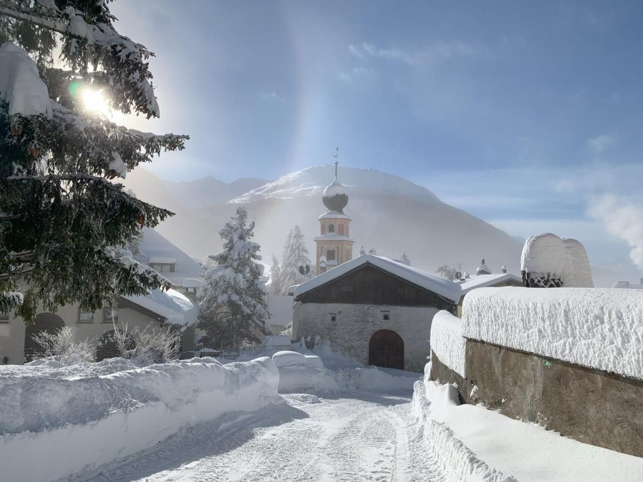 En snøklædt landsby med en kirke og bjerge i baggrunden.