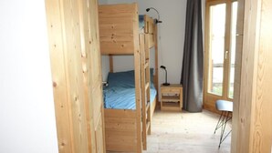Ein Zimmer mit einem Holzbett mit Etagen, einem Schreibtisch und einem Stuhl, einem Fenster mit Vorhängen und einer Tür.
