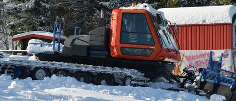 A snowplow truck parked in a snowy area with a red building in the background.
