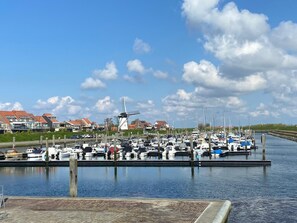 Ein Yachthafen mit vertäuten Booten, einer Windmühle und Häusern im Hintergrund.