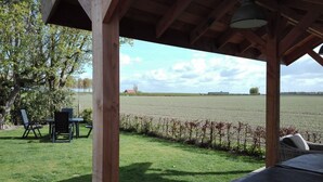 Puinen pergola, josta avautuu näkymä pellolle ja kauempana sijaitsevaan rakennukseen.