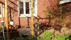A brick house with a wooden pergola, a garden with potted plants, and outdoor furniture. - in Norden mit großem Garten by Interhome (Norden)