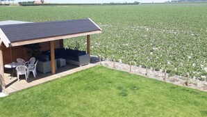 Ein überdachter Außenbereich mit Tisch und Stühlen, mit Blick auf ein großes Feld.