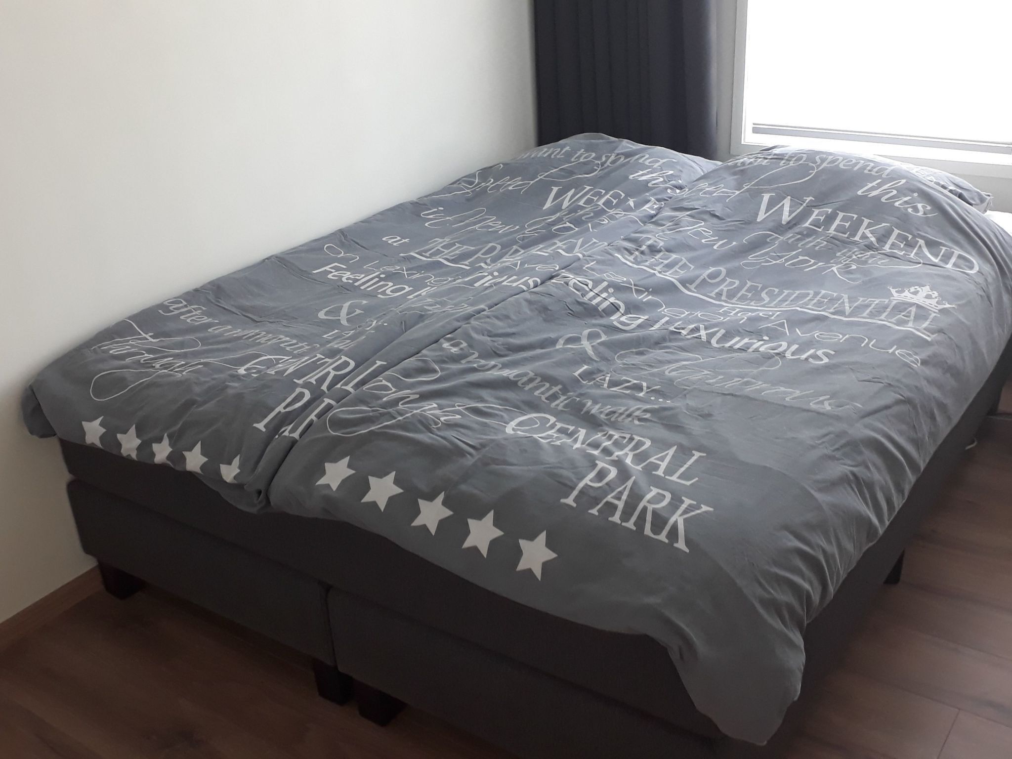 Un lit recouvert d’une couvre-lit grise ornée de motifs blancs représentant des étoiles et du texte.