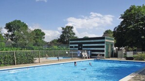 Ein rechteckiger Pool mit Fliesenrand, umgeben von einem Zaun und Bäumen.