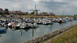 Ein Yachthafen mit zahlreichen Booten, ein Windmühlengrund im Hintergrund und Häuser entlang des Ufers.