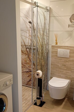 A modern bathroom with a glass shower enclosure, a toilet, and a washing machine. - Ferienhaus 13 mit großem Wintergarten by Interhome (Stavenisse)