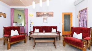 Een kamer met twee rode fluweelzitzaken, een houten salontafel en een stadsgezichtschilderij aan de muur.