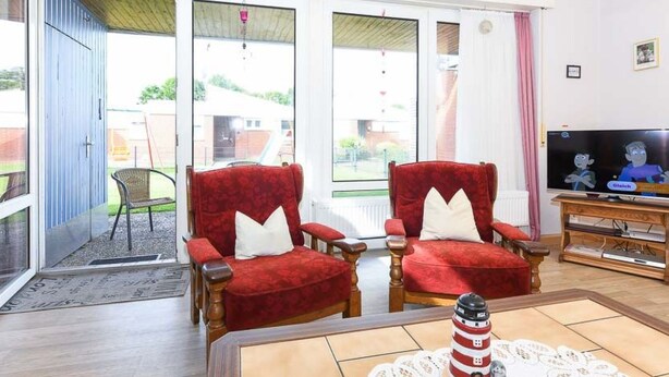Een woonkamer met twee rode fauteuils, een houten salontafel, een televisie en een klein model van een vuurtoren.