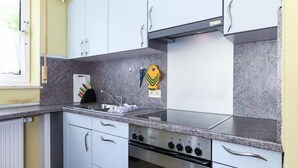 Een kleine keuken met witte kastjes, een roestvrijstalen fornuis en een raam met gordijnen.
