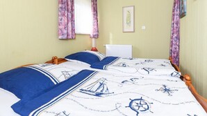 Een slaapkamer met twee bedden, bloemen gordijnen, een radiator en beddengoed met een nautisch thema.