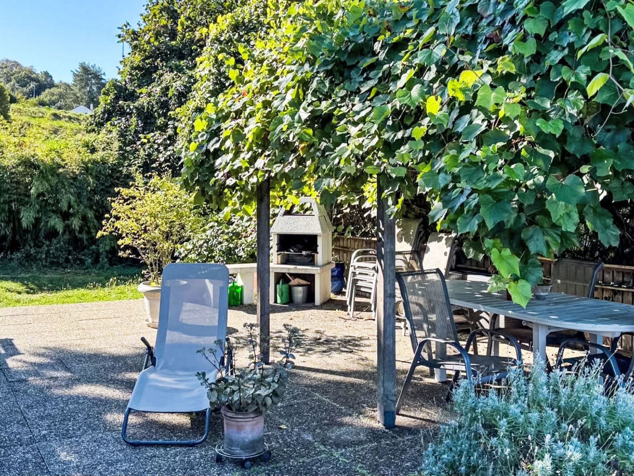 Ein Terrassenbereich im Freien mit Tisch und Stühlen, einer überdachten Sitzgelegenheit und einem Blumentopf.
