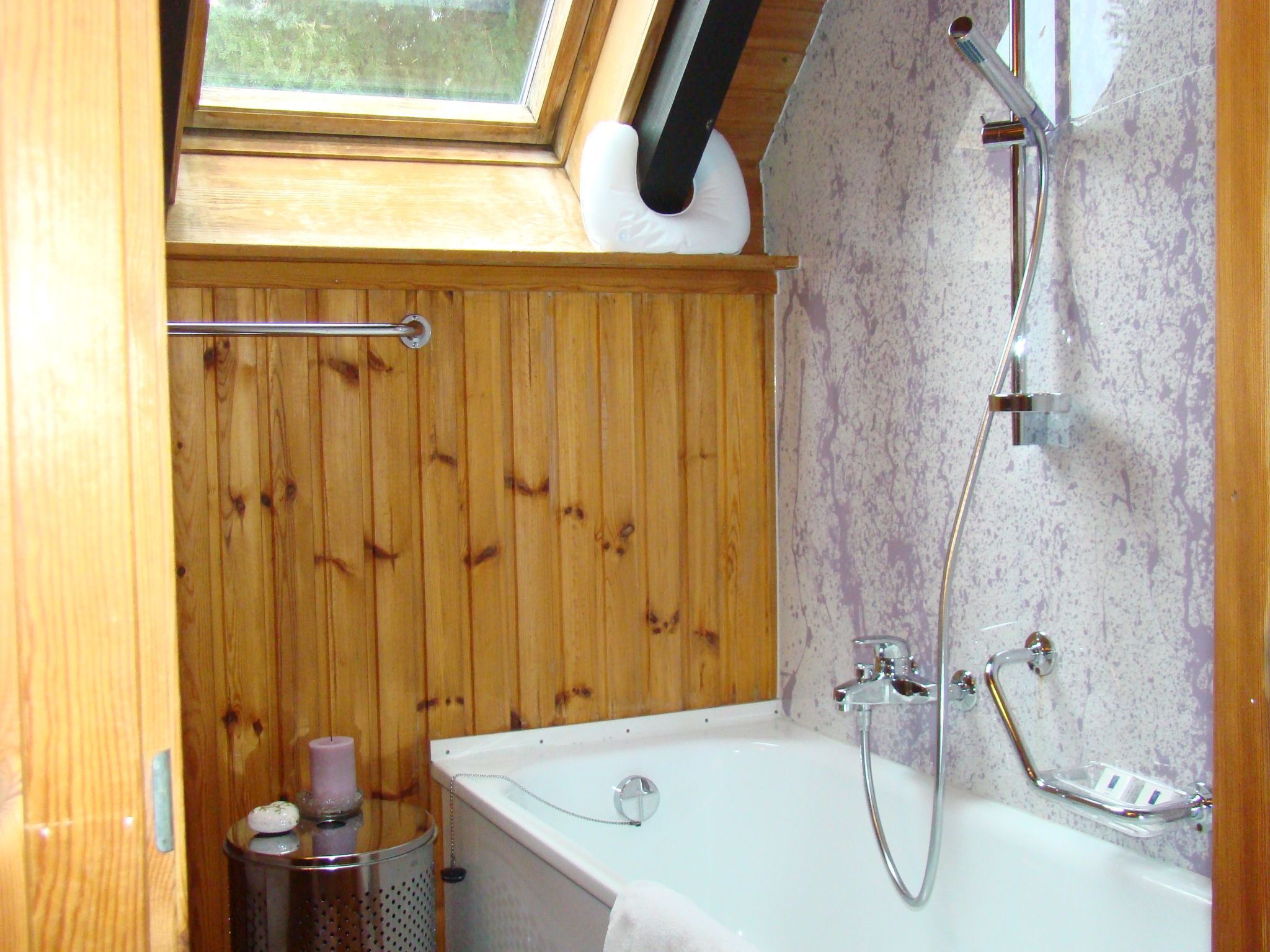 Un baño pequeño con tragaluz, paneles de madera, una bañera blanca, ducha y un cubo de basura.