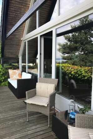 Eine Terrasse im Freien mit Korbmöbeln, einer Glastür, die zum Innenbereich führt, und Blick ins Grüne.