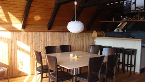 Een eethoek met een houten tafel en stoelen, een hanglamp en een keuken op de achtergrond.