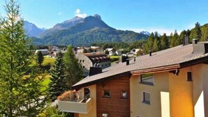 A mountain village with traditional wooden houses, a clear sky, and a prominent mountain peak in the background.