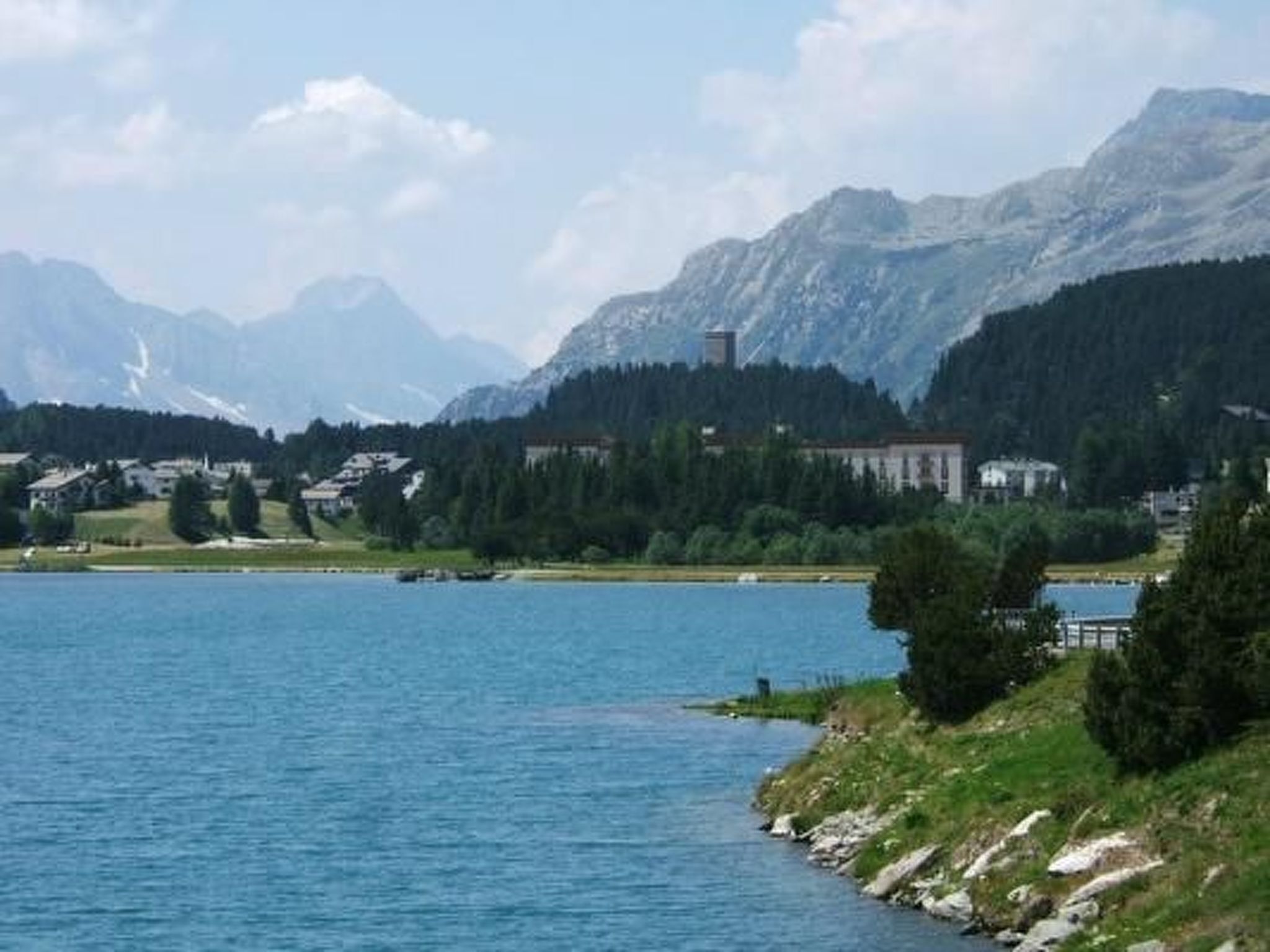 Un lac avec une chaîne de montagnes en arrière-plan, un bâtiment avec un toit rouge et un petit quai.