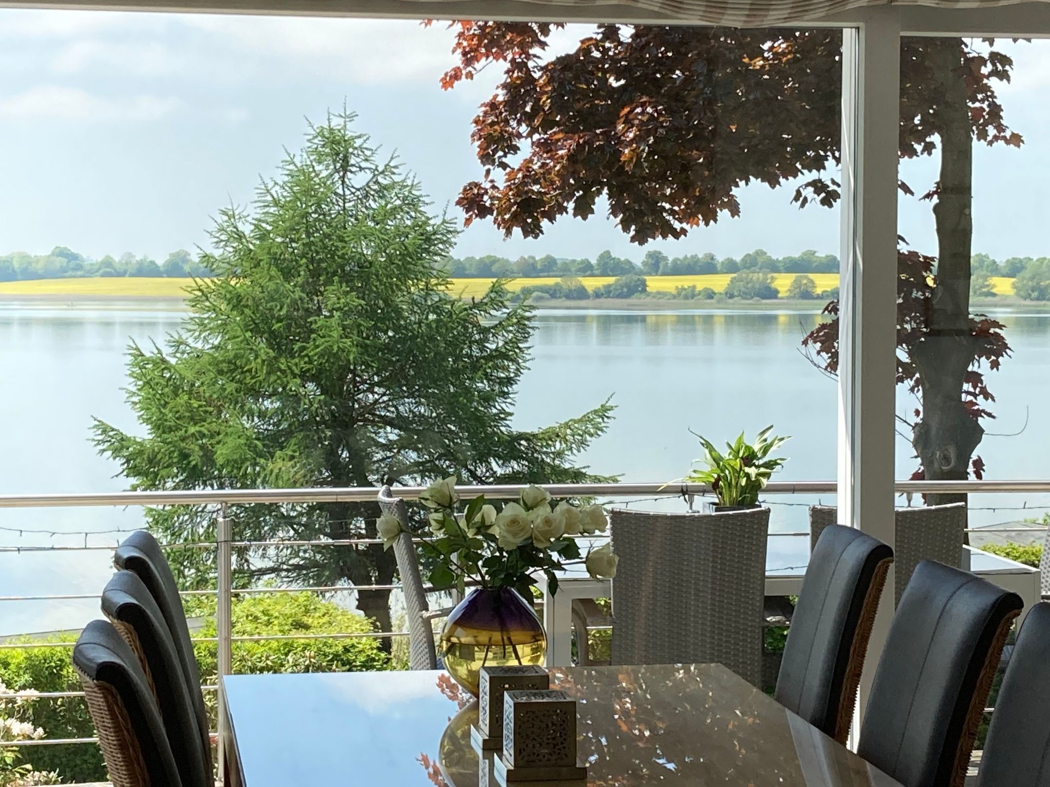 Uma área de refeições com vista para um lago, mobiliário ao ar livre e uma mesa com cadeiras.
